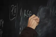 Учител пише с тебешир на черна дъска